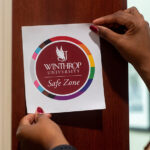 Photo of a Winthrop Safezones sticker, held up by two hands which belong to a African American person