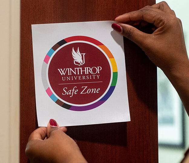 Photo of a Winthrop Safezones sticker, held up by two hands which belong to a African American person